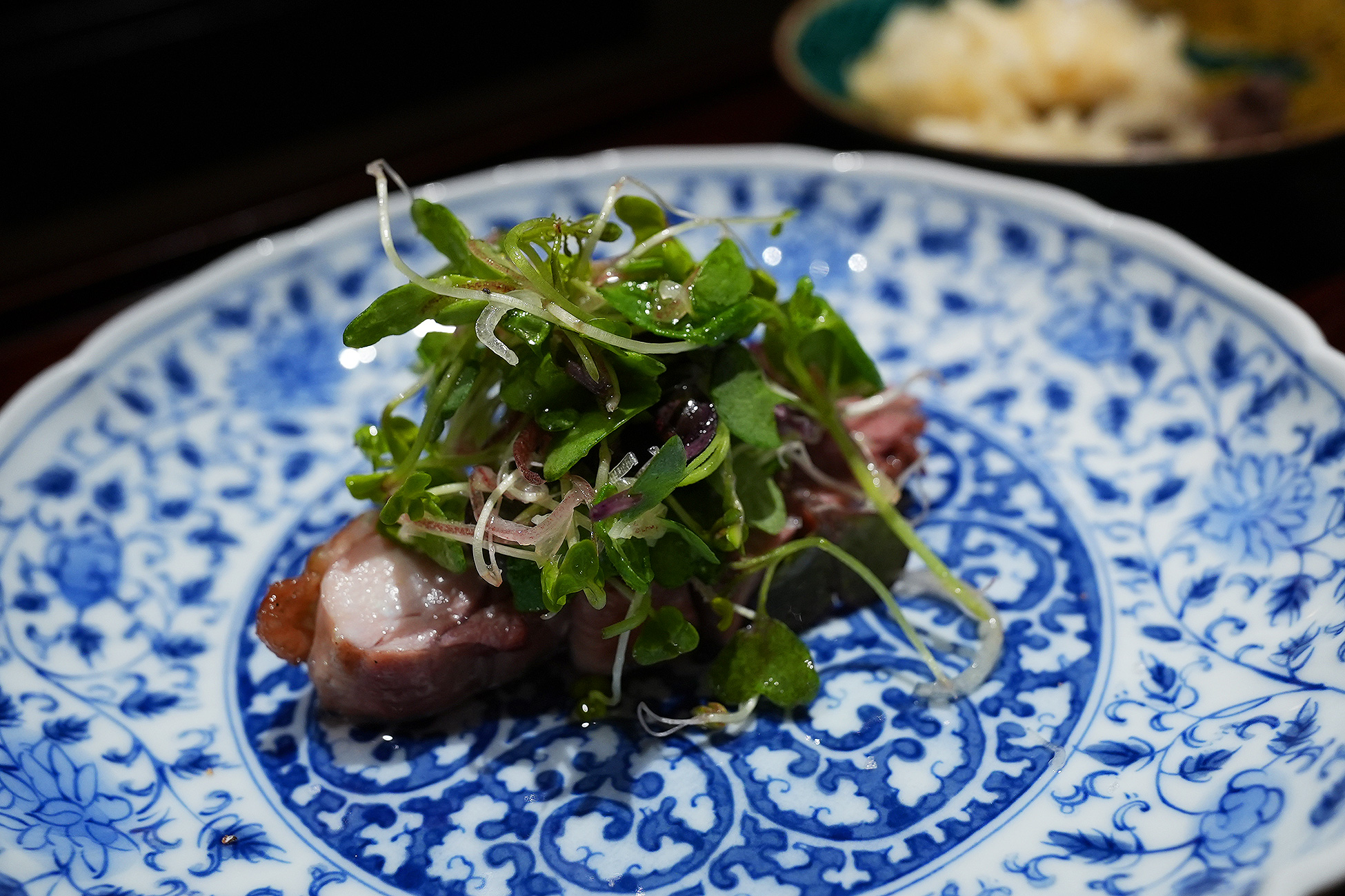 青い染付の皿に、焼いた鶏肉と茗荷や水菜、赤大根、紫蘇の芽がたっぷり盛られている