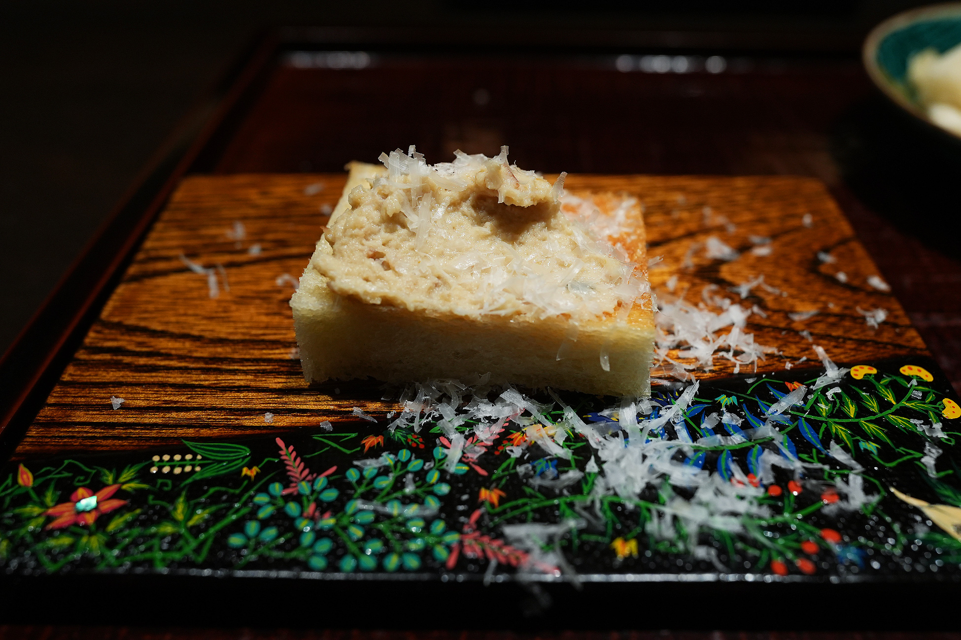 草花を描いた黒い盆の上に、断面を見せて置かれた薪焼きのパン。細い鶏節が散らしてある