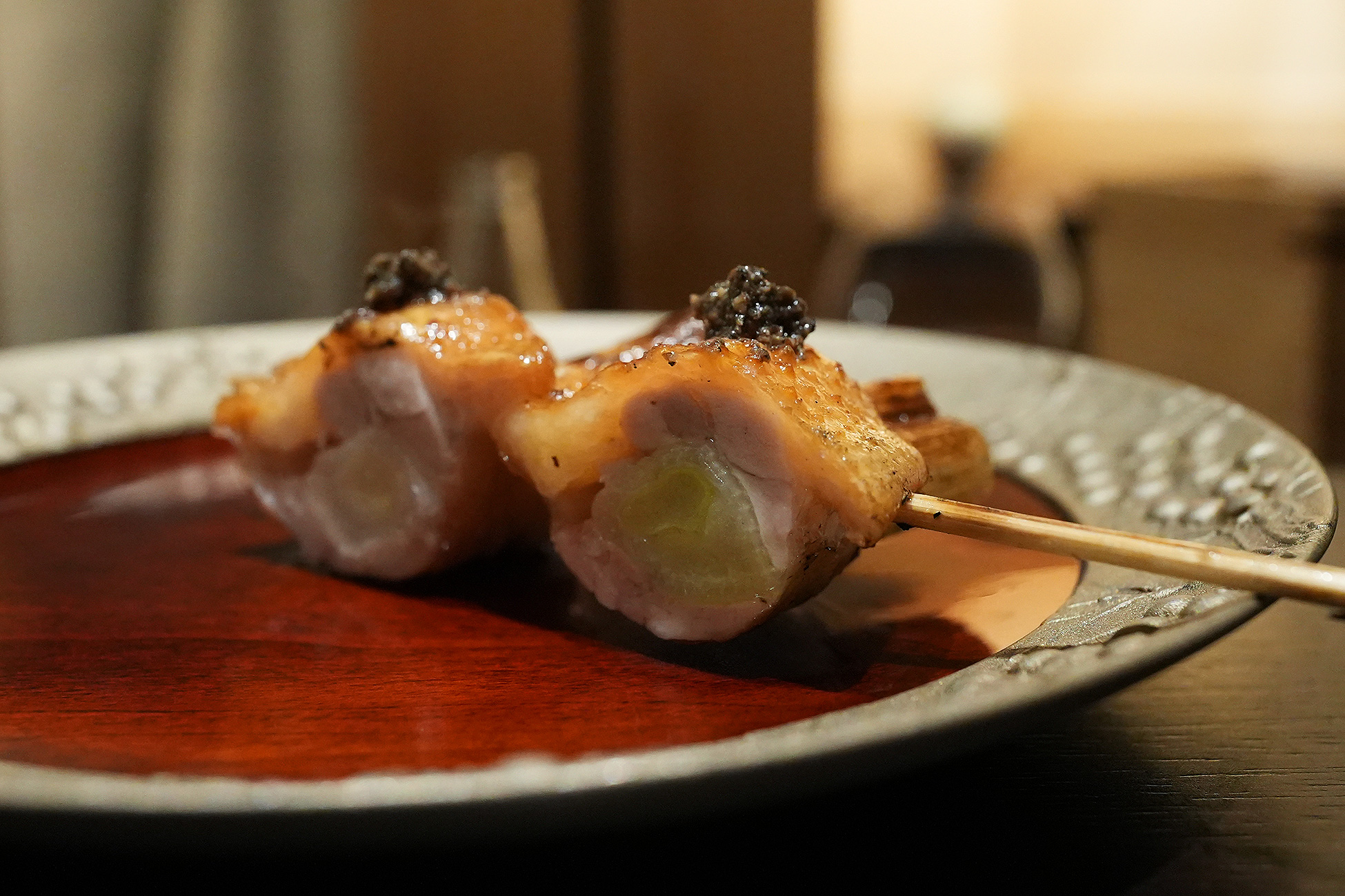 銀色の皿の上に置かれた串。大ぶりの手羽肉の間に葱がのぞき、黒い生胡椒がのっている