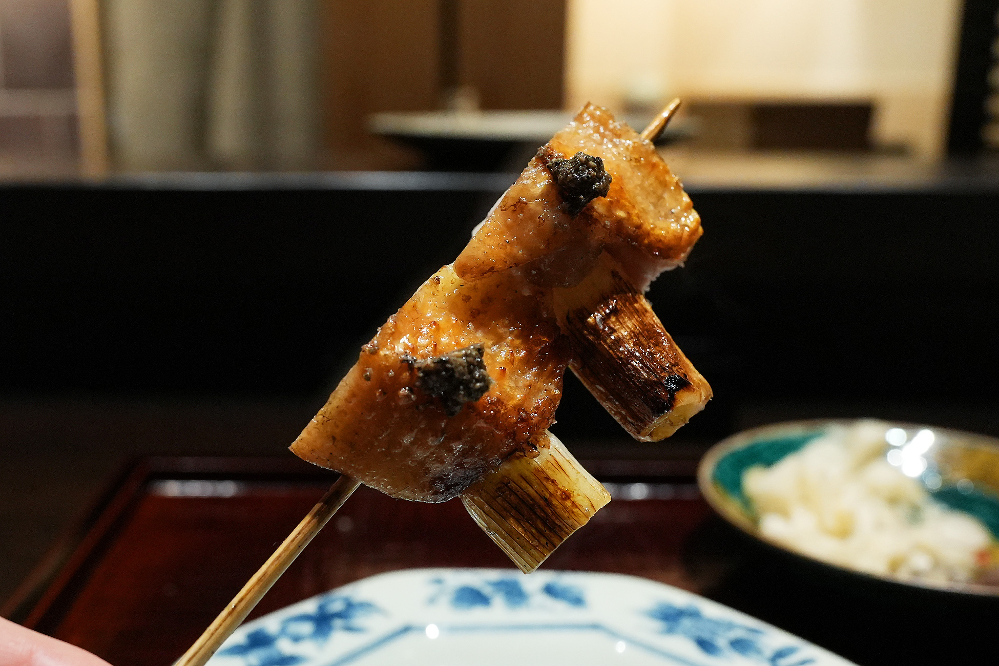 手に持った串を横から見たところ。手羽肉の間に白い葱がはっきり見え、表面に黒い生胡椒がのる