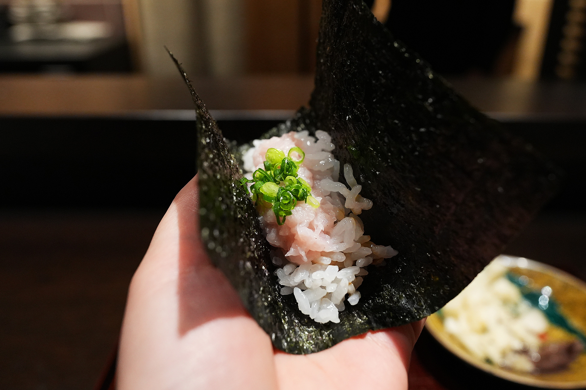 手に持った海苔巻き。酢飯の上に細かくたたいた鶏肉がのり、青葱が散らしてある