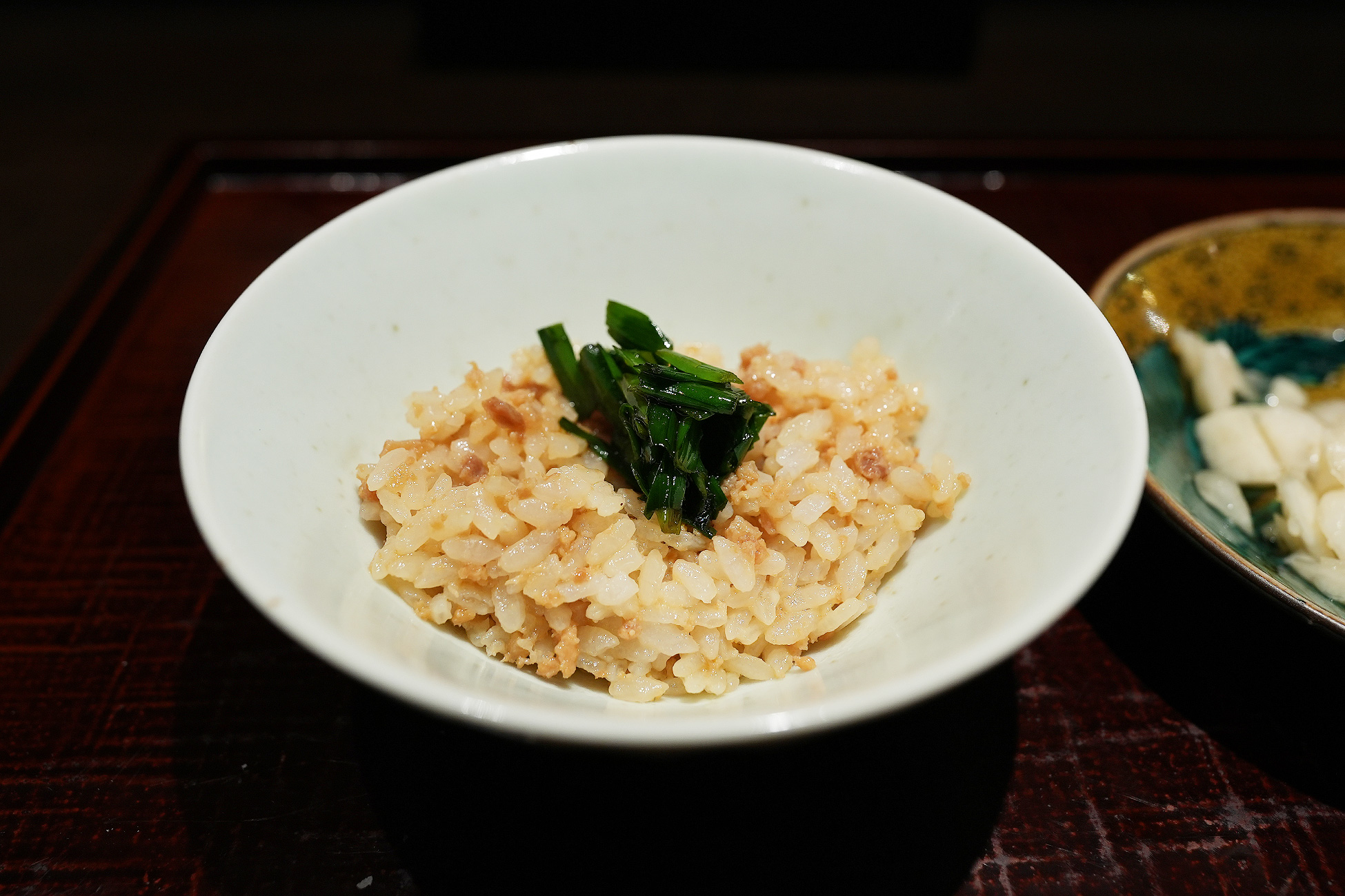 白い小鉢によそわれたご飯の上に、鶏そぼろがたっぷり。中央に緑の韮がのっている