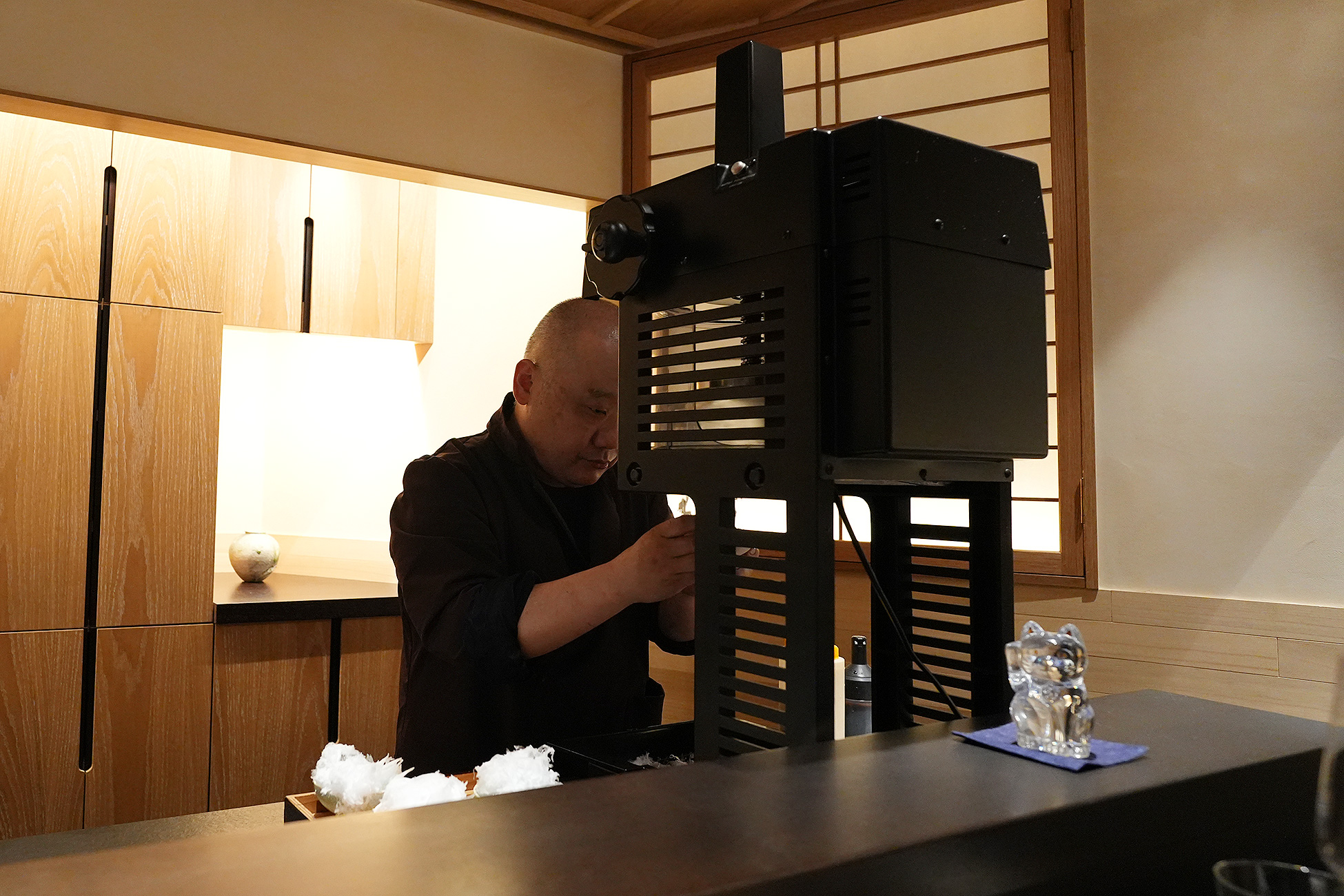 黒いかき氷機に向かう店主。カウンターの端に招き猫が置かれている