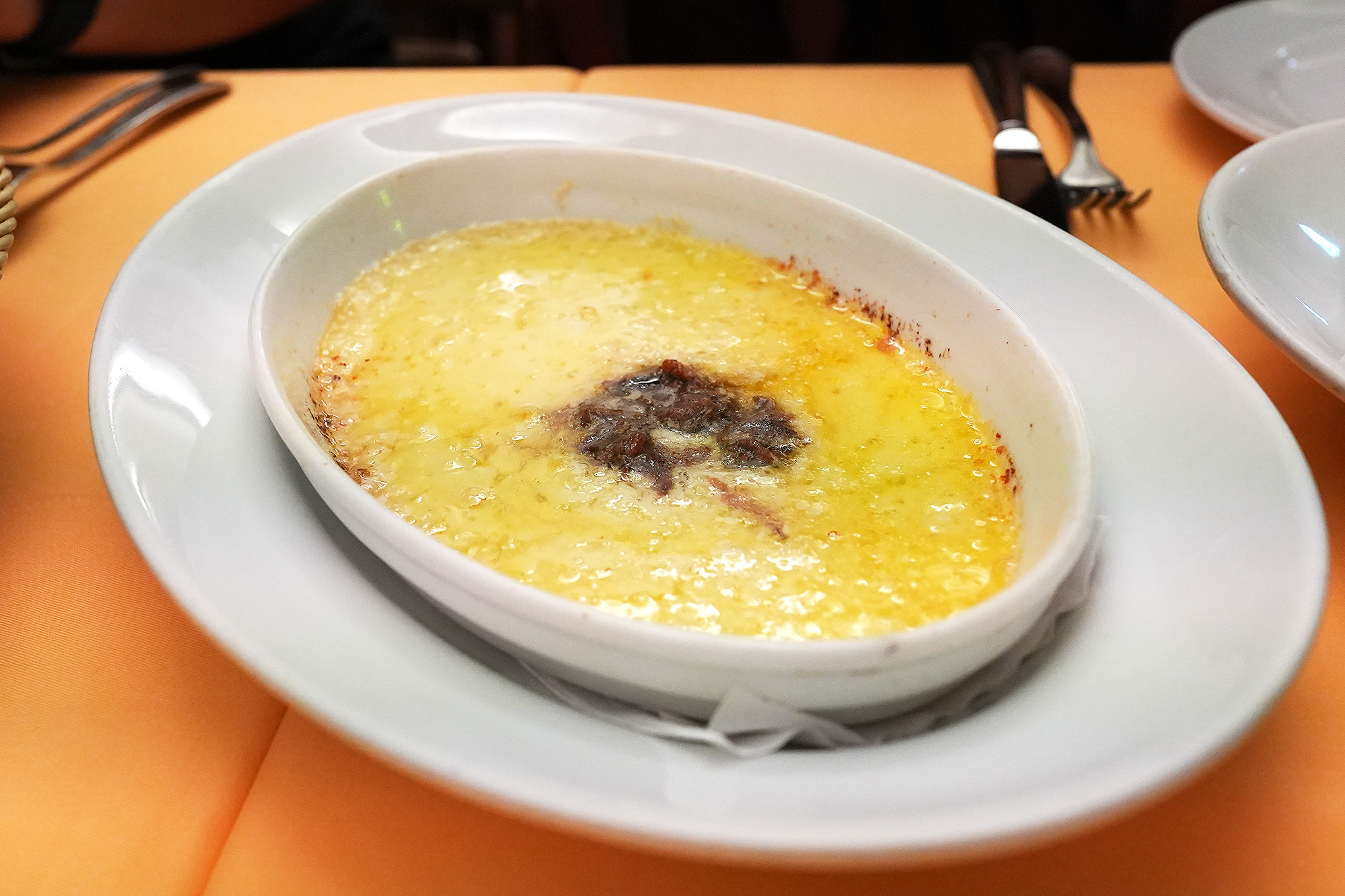 グラタン皿で焼かれた、こんがりと焦げ目のついたペコリーノチーズ。中央にアンチョビがのっている