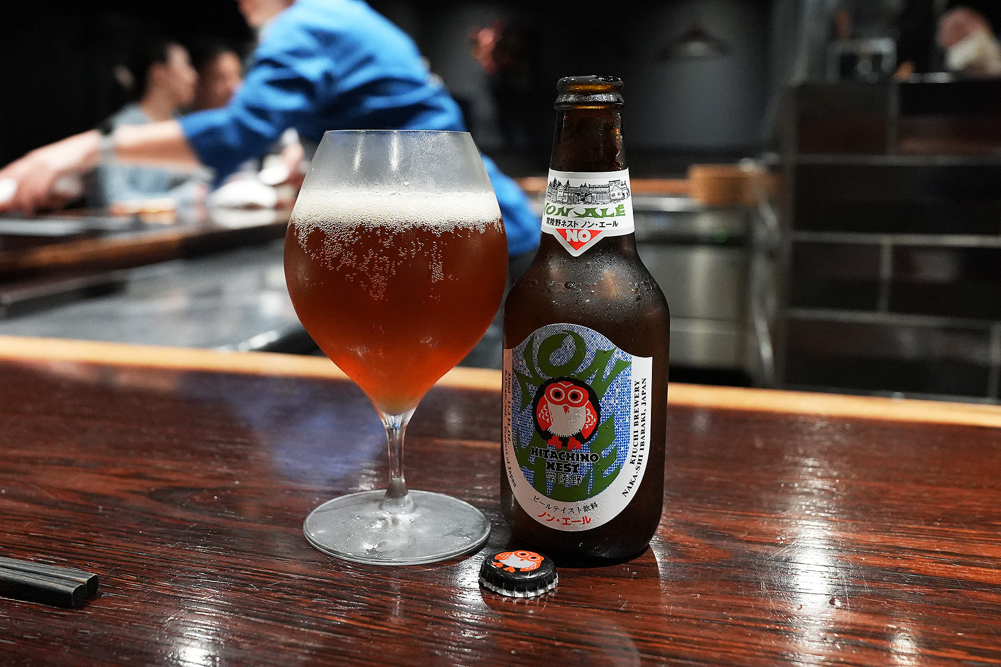 カウンターに置かれた常陸野ネストビールの瓶と、琥珀色の液体が注がれたグラス。ラベルにはフクロウの絵と「ノン・エール」の文字