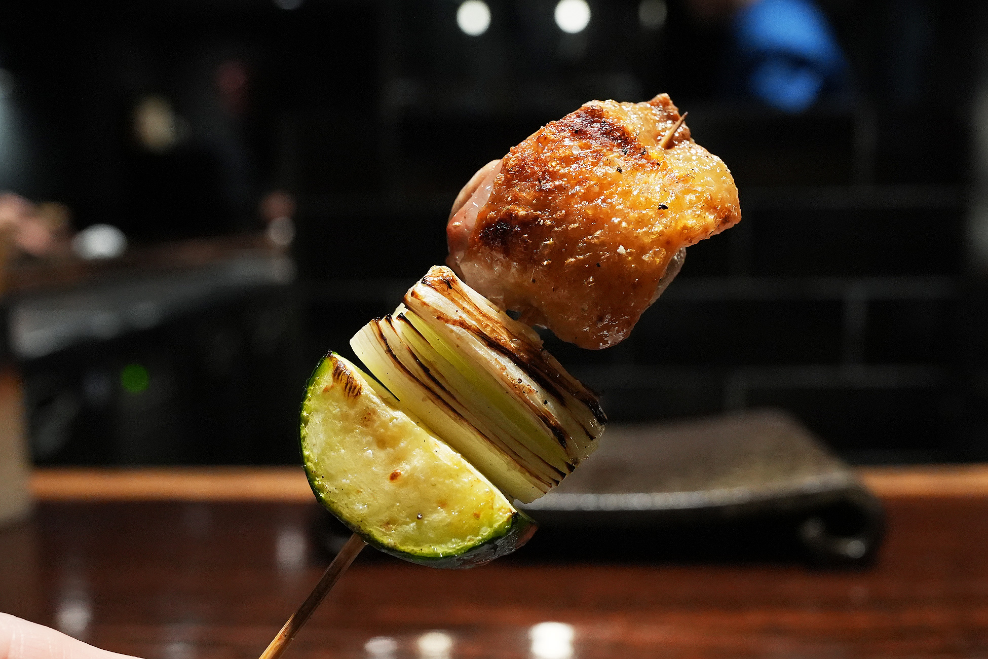 串に刺さったホロホロ鳥のソリ。皮目がこんがり焼け、下に焼いた葱とズッキーニが刺さっている